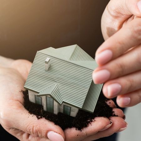 Manos cogiendo una pequeña casa de cartón