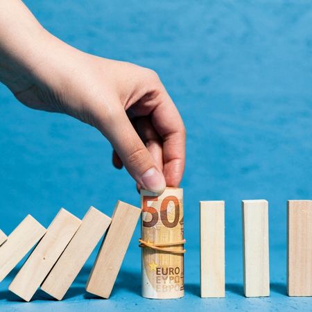 Piezas de madera cayendo y una mano sujetando un rollo de billetes de 50€