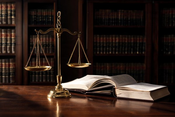 Balanza de la justicia de latón junto a libros de jurisprudencia en una biblioteca jurídica.