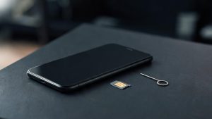 Un teléfono móvil junto a una tarjeta SIM extraída sobre una mesa de oficina con iluminación tenue.