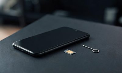 Un teléfono móvil junto a una tarjeta SIM extraída sobre una mesa de oficina con iluminación tenue.