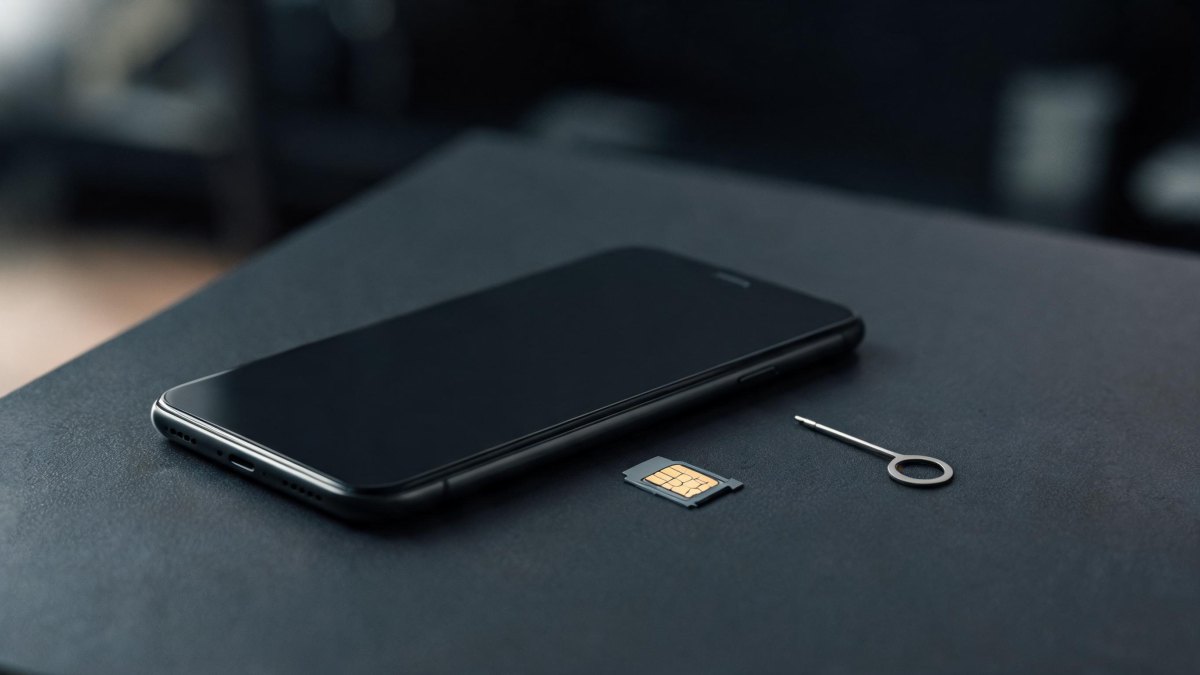 Un teléfono móvil junto a una tarjeta SIM extraída sobre una mesa de oficina con iluminación tenue.
