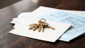 Llaves de una vivienda colocadas sobre documentos fiscales y planos residenciales en un escritorio.