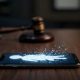 Teléfono inteligente sobre una mesa mostrando una figura digital abstracta junto a un mazo judicial desenfocado