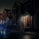 Exterior de una vivienda en una calle nocturna con señales de humo y luces de emergencia reflejadas.