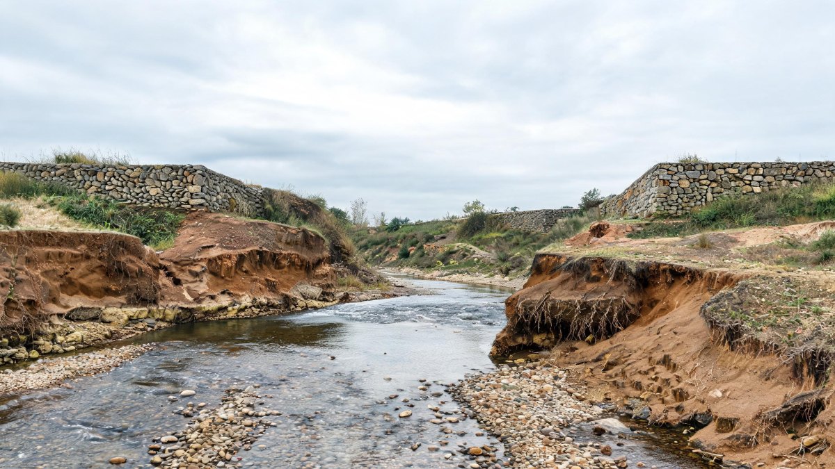 Cauce de un arroyo con erosión natural en sus márgenes y obras de contención