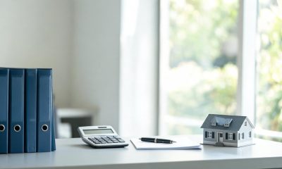 Documentos financieros, pluma estilográfica y maqueta de una casa sobre una mesa de madera de un despacho legal.