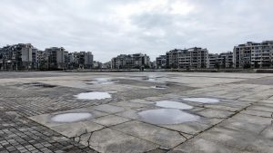 Suelo de una plaza comunitaria con encharcamientos y fisuras superficiales tras la lluvia.