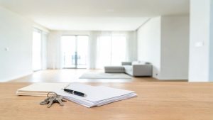 Mesa de madera con documentos legales y llaves en el interior de una vivienda vacía y luminosa.